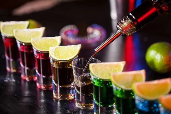 小さなグラスに酒を注ぐバーテンダーのバー バーではカラフルなカクテル クラブでカラフルなショット 異なる色のアルコール飲料です ナイトライフ シーン バーでショット テーブル — ストック写真