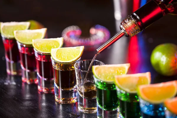 小さなグラスに酒を注ぐバーテンダーのバー バーではカラフルなカクテル クラブでカラフルなショット 異なる色のアルコール飲料です ナイトライフ シーン バーでショット テーブル — ストック写真