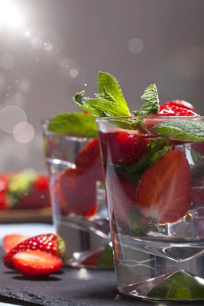 Çilek, nane ve buz cam siyah arka plan üzerine yaz soğuk içecek. Taze berry meyve ile kokteyller closeup.