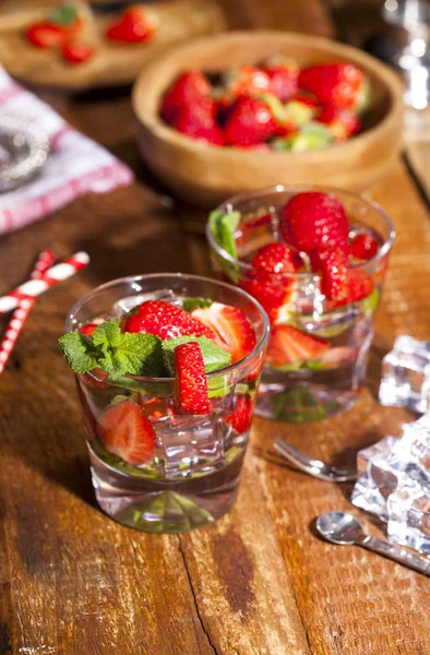 Çilek, nane ve buz cam ahşap zemin üzerine yaz soğuk içecek. Taze berry meyve ile kokteyller closeup.