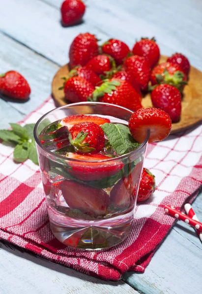 Çilek, nane ve buz cam mavi ahşap zemin üzerine yaz soğuk içecek. Taze berry meyve ile kokteyller closeup.