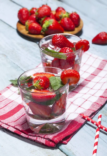 Çilek, nane ve buz cam mavi ahşap zemin üzerine yaz soğuk içecek. Taze berry meyve ile kokteyller closeup.