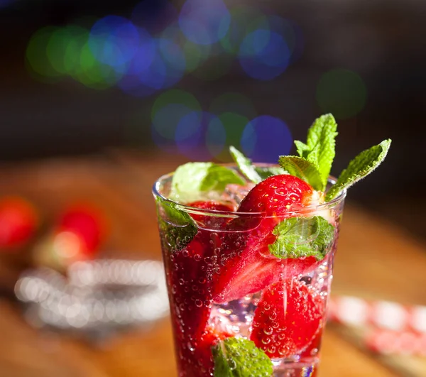 Çilek, nane ve buz cam üstünde ahşap bar sayaç ile yaz soğuk içecek. Closeup taze berry meyve kokteyli.