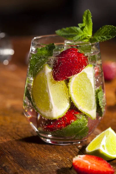Çilek, nane, limon ve buz cam üstünde ahşap bar sayaç ile yaz soğuk içecek. Closeup taze berry meyve kokteyli.