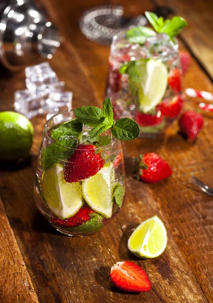 Çilek, nane, limon ve buz cam üstünde ahşap bar sayaç ile yaz soğuk içecek. Closeup taze berry meyve kokteyli.