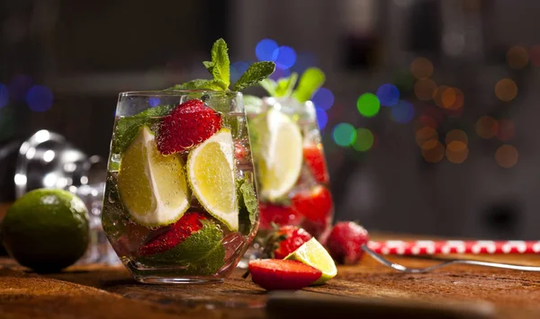 Çilek, nane, limon ve buz cam üstünde ahşap bar sayaç ile yaz soğuk içecek. Closeup taze berry meyve kokteyli.
