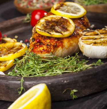 Taze kekik, kiraz domates, limon, sarımsak ve baharat kayrak bir plaka üzerinde siyah bir arka plan ile ızgara tavuk fileto