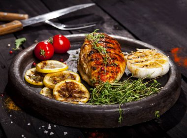 Taze kekik, kiraz domates, limon, sarımsak ve baharat kayrak bir plaka üzerinde siyah bir arka plan ile ızgara tavuk fileto