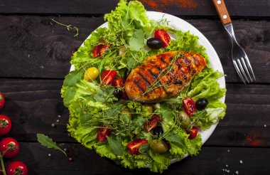 Taze marul, kekik, kiraz domates ve siyah bir zemin üzerine bir tabak içinde zeytin ızgara tavuk fileto