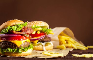 Sığır eti, domates, peynir, salatalık, soğan, marul ahşap masa ve kopya alanı ile kahverengi zemin üzerine iki farklı lezzetli burger