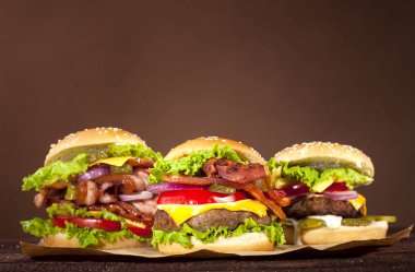 Sığır eti, domates, peynir, salatalık, soğan, marul ahşap masa ve kopya alanı ile kahverengi zemin üzerinde üç farklı lezzetli burger