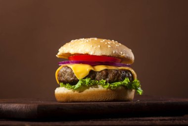 Sığır eti, domates, peynir, soğan, marul ahşap masa ve kopya alanı ile kahverengi zemin üzerine taze lezzetli burger