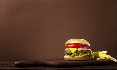 Sığır eti, domates, peynir, soğan, marul ahşap masa ve kopya alanı ile kahverengi zemin üzerine taze lezzetli burger