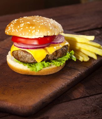 Sığır eti, domates, peynir, soğan, marul ahşap masa ve kahverengi zemin üzerine taze lezzetli burger