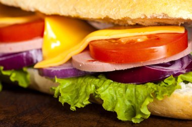 Jambon, peynir, marul, domates ve soğan bir kesme tahtası üzerinde bir baget sandviç closeup. Karanlık bir arka plan üzerinde uzun Metro sandviç.