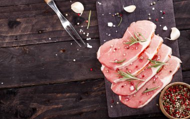 Çiğ et. Biberiye ve baharat kopya alanı ile siyah bir arka plan ile bir kesme tahtası üzerinde ham sığır eti biftek.