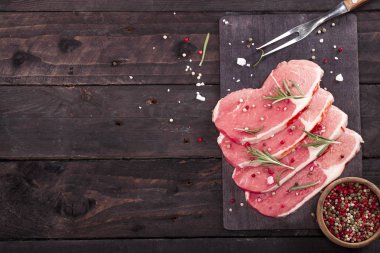 Çiğ et. Biberiye ve baharat kopya alanı ile siyah bir arka plan ile bir kesme tahtası üzerinde ham sığır eti biftek.