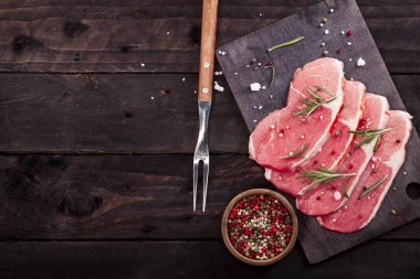 Çiğ et. Biberiye ve baharat kopya alanı ile siyah bir arka plan ile bir kesme tahtası üzerinde ham sığır eti biftek.