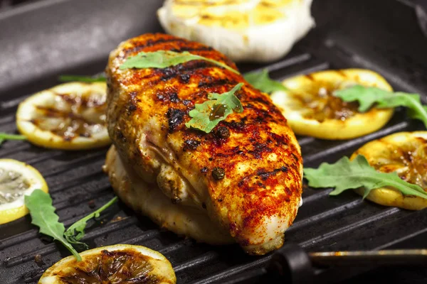 Grilled chicken fillet with spices and fresh vegetables in a pan on a black background