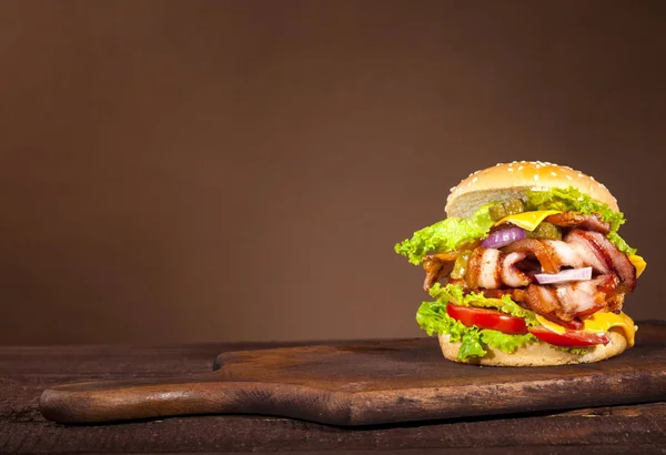 Fresh delicious big burger with bacon, tomato, cheese, cucumber, onion and lettuce on wooden background with copy space