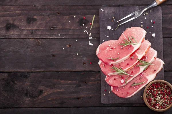 Çiğ et. Biberiye ve baharat kopya alanı ile siyah bir arka plan ile bir kesme tahtası üzerinde ham sığır eti biftek.