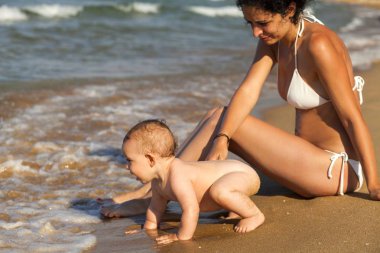 Anne ve bebek oğlu altın sahilde suda oynamak.
