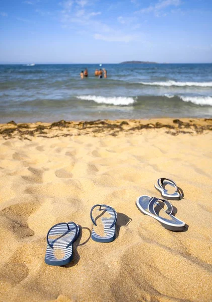 Блакитне сандалове перевертання на піщаному пляжі і група граючих людей на відстані у воді — стокове фото
