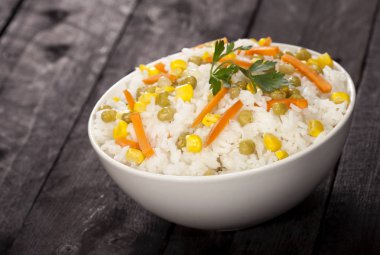 Ahşap siyah arka plan üzerine bir kase sebze ile beyaz pirinç pişmiş.