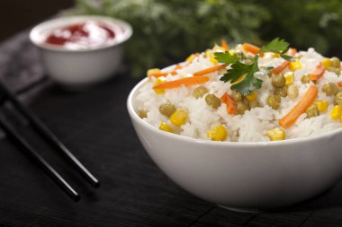 Soslar ve chopsticks ahşap bambu siyah arka plan üzerine bir kase sebze ile beyaz pirinç pişmiş.