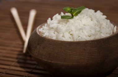 Ahşap kahverengi bambu zemin üzerine yemek çubukları ile ahşap kase beyaz pirinç pişmiş.