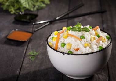 Soslar ve chopsticks ahşap siyah arka plan üzerine bir kase sebze ile beyaz pirinç pişmiş.