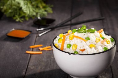 Soslar ve chopsticks ahşap siyah arka plan üzerine bir kase sebze ile beyaz pirinç pişmiş.