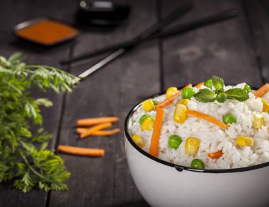 Soslar ve chopsticks ahşap siyah arka plan üzerine bir kase sebze ile beyaz pirinç pişmiş.