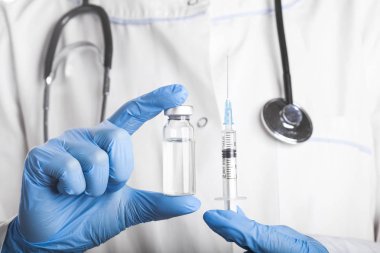 Bir şırınga ve iğne çözümünü bir şişeyle tutan doktor