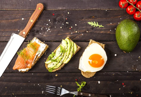 Drie verschillende bruschettas met avocado, rucola, sesamzaad, zaden, ei, zalm op houten tafel — Stockfoto