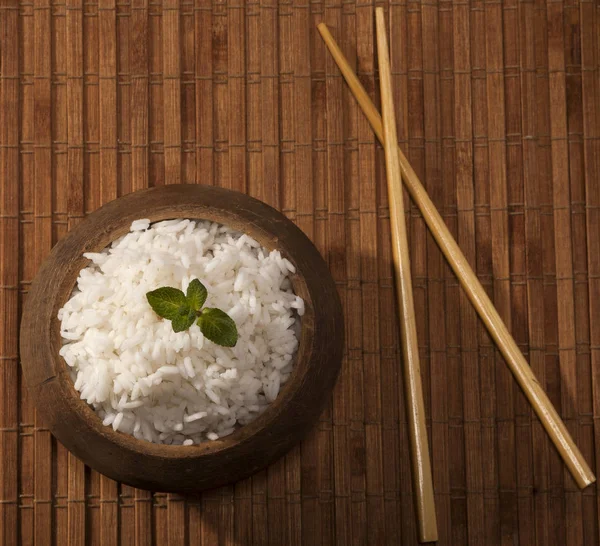 Arroz blanco cocido en tazón de madera con palillos en el fondo de bambú marrón madera . — Foto de Stock