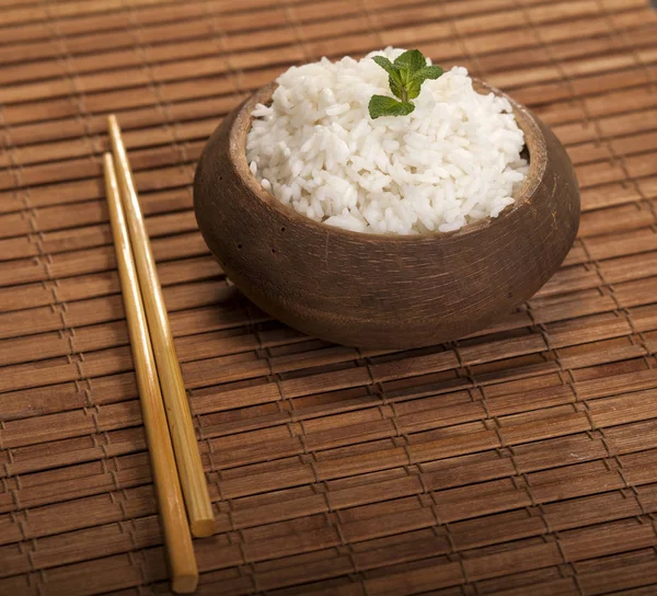 Arroz blanco cocido en tazón de madera con palillos en el fondo de bambú marrón madera . — Foto de Stock