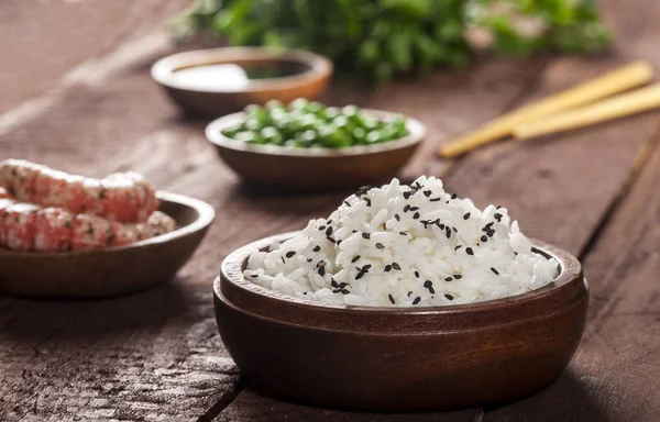 Vařená bílá rýže v dřevěné misce s krevetkami, hrášek, sezamu a hůlky na dřevo hnědé pozadí. — Stock fotografie