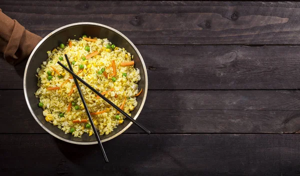 Gekookte rijst met curry en groenten in een pan met stokjes op de houten zwarte achtergrond. — Stockfoto