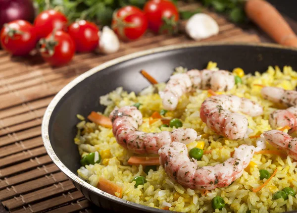 Gekookte rijst met garnalen, curry en groenten in een pan op de achtergrond hout bruin bamboe. — Stockfoto