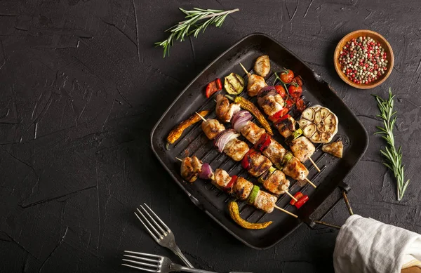 Grillade kycklingspett med kryddor och grönsaker i en kastrull på svart bakgrund — Stockfoto