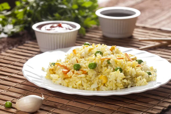 Μαγειρεμένο ρύζι με κάρυ και λαχανικά σε ένα πιάτο με σάλτσες και chopsticks στο ξύλο Μπαμπού καφέ φόντο. Royalty Free Φωτογραφίες Αρχείου