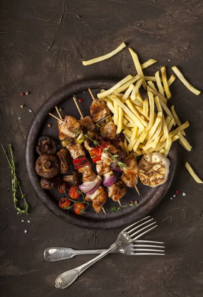 Espetos de frango grelhados com especiarias, legumes e batatas fritas em uma panela no fundo preto Fotografia De Stock