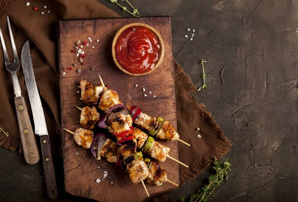 Grillade kycklingspett med kryddor och grönsaker på skärbräda och mörk bakgrund — Stockfoto