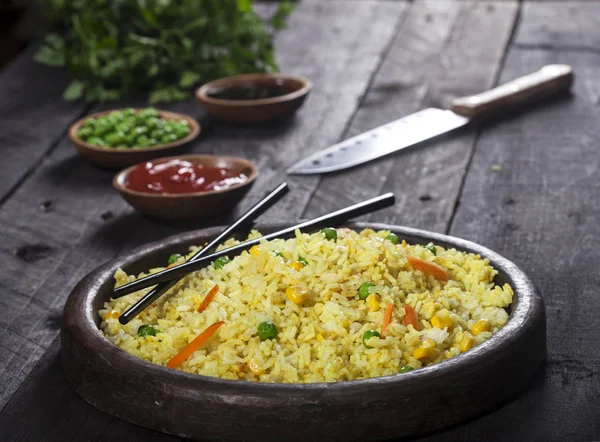 Gekookte rijst met curry en groenten in een pan met stokjes op de houten zwarte achtergrond. — Stockfoto