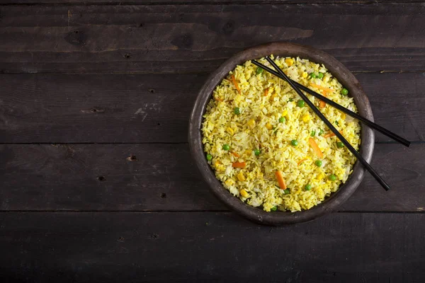 Gekookte rijst met curry en groenten in een pan met stokjes op de houten zwarte achtergrond. — Stockfoto