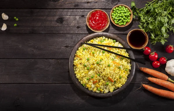 Gekookte rijst met curry en groenten in een pan met stokjes op de houten zwarte achtergrond. — Stockfoto