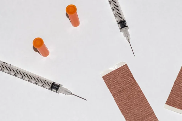 two insulin syringes with their needles and caps and two strips on a white background