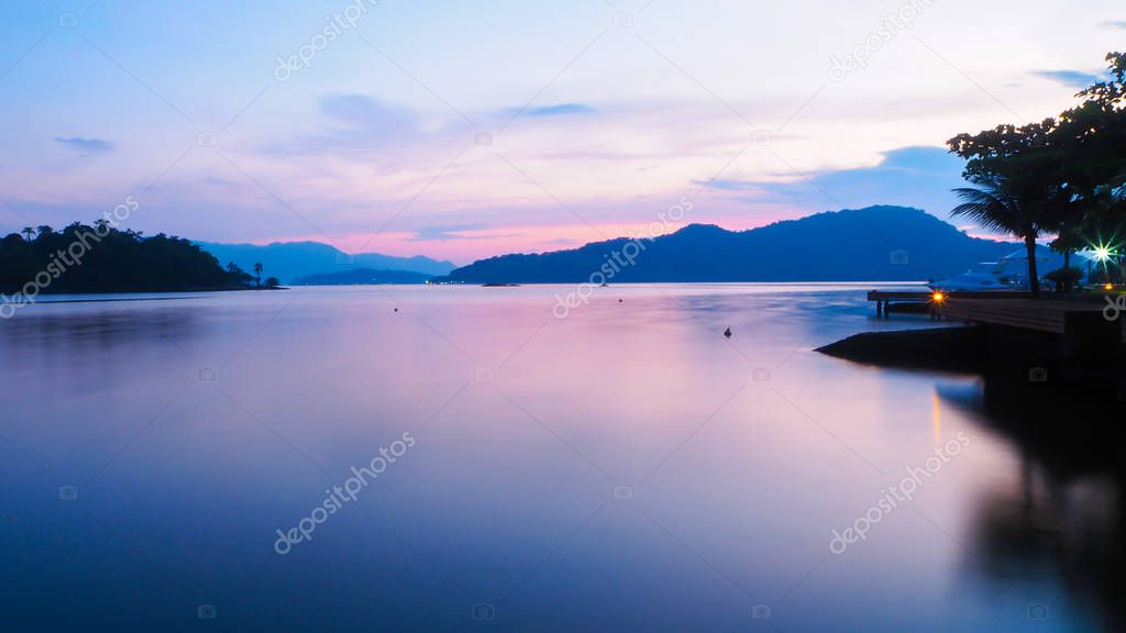 Beautiful violet sunset with reflexions in the motionless ocean - Island and hills in the background 