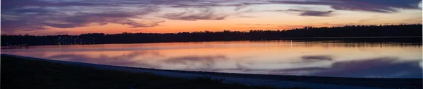 Gölde günbatımında panoramik manzara. Romantik dalgalar, ön planda kıyılar ve arkada orman.